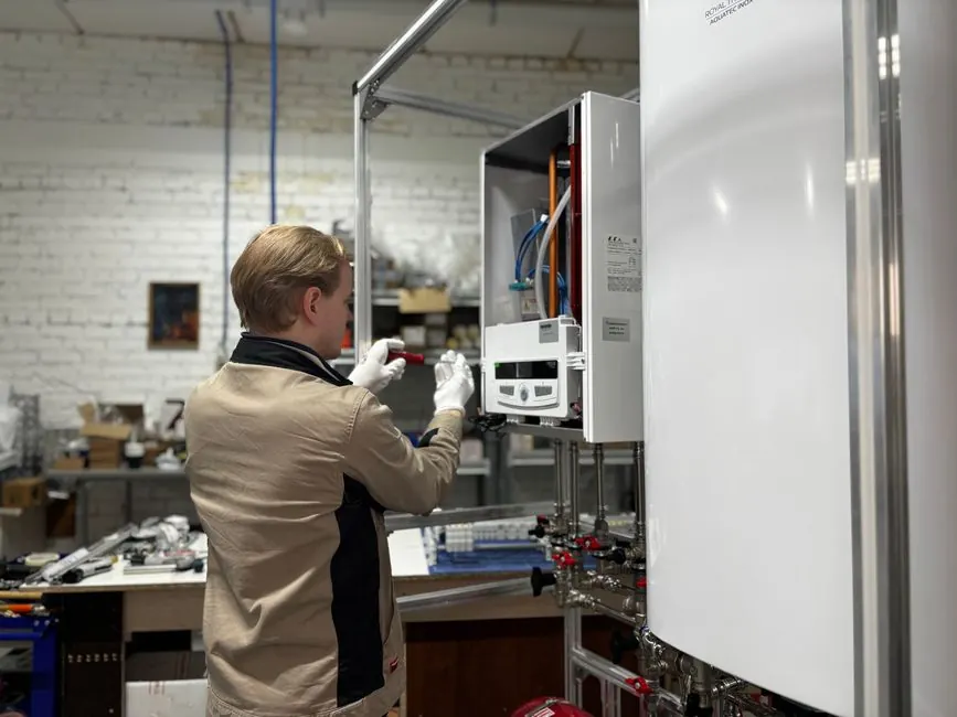 Technician inspects and repairs a heating system in an industrial workshop setting.